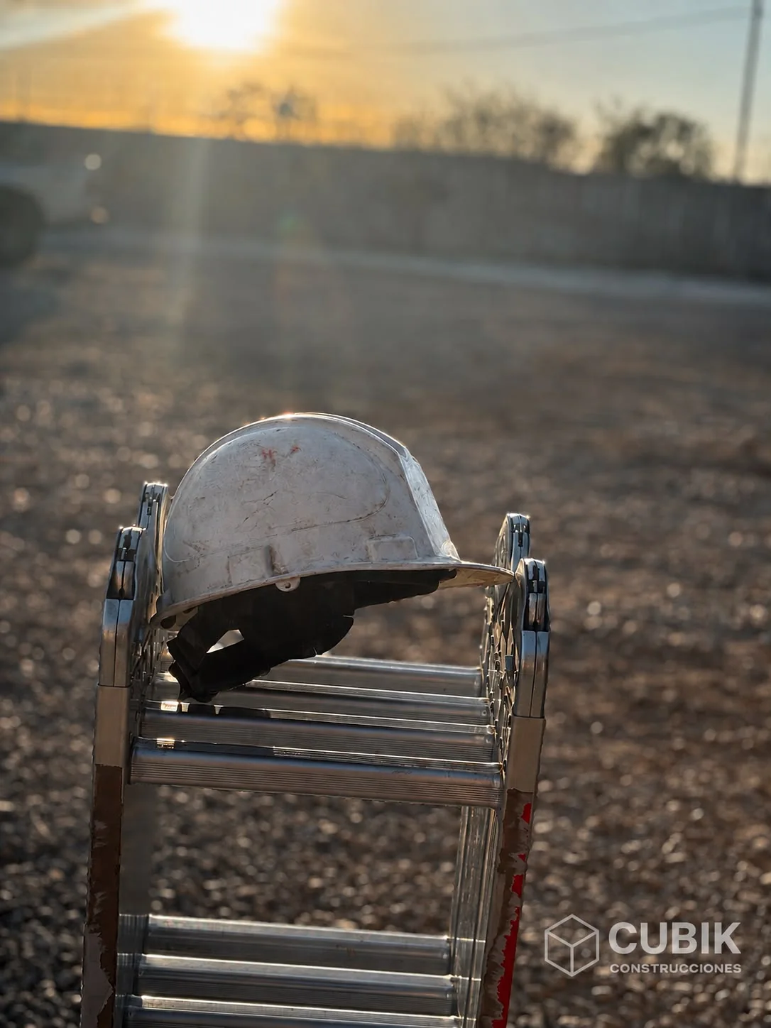 Casco de seguridad apoyado sobre una escalera en una obra, con luz de atardecer